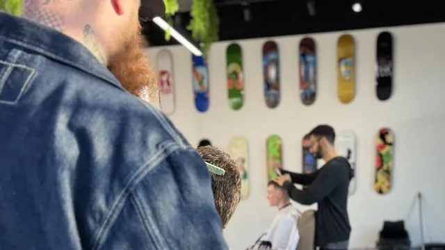 Barbers at work in the shop, skateboard decks along the wall