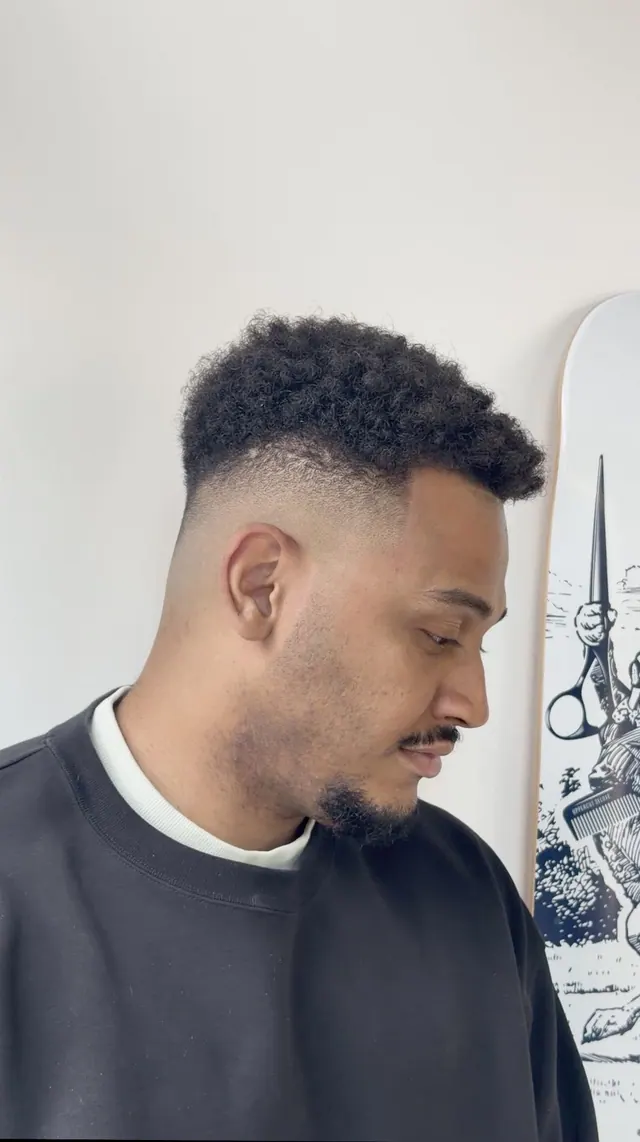 A curly top with a skin fade and a shaped beard